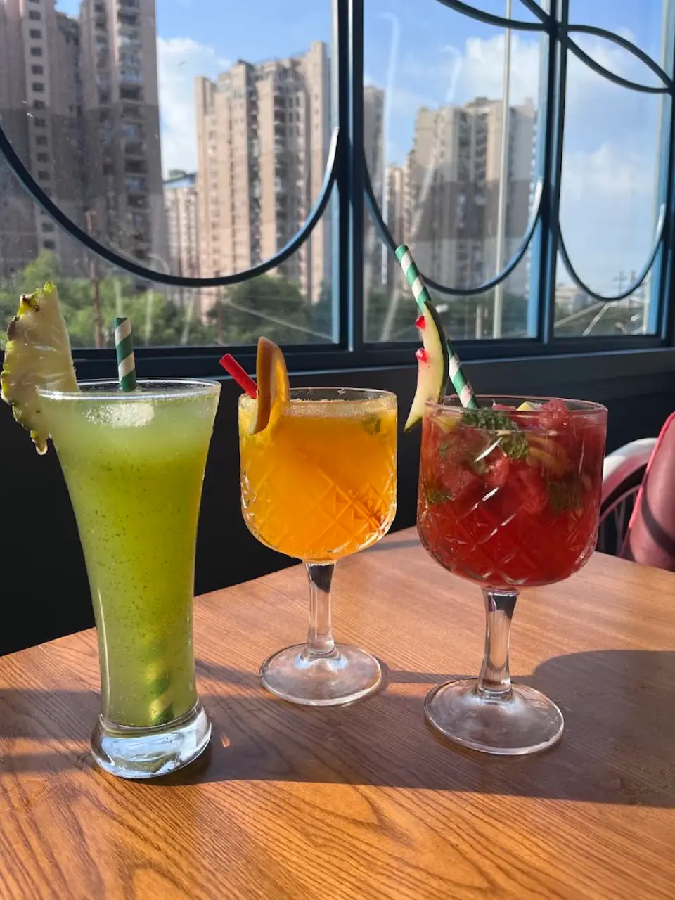 Three fresh mocktails on a wooden table by a sunny window