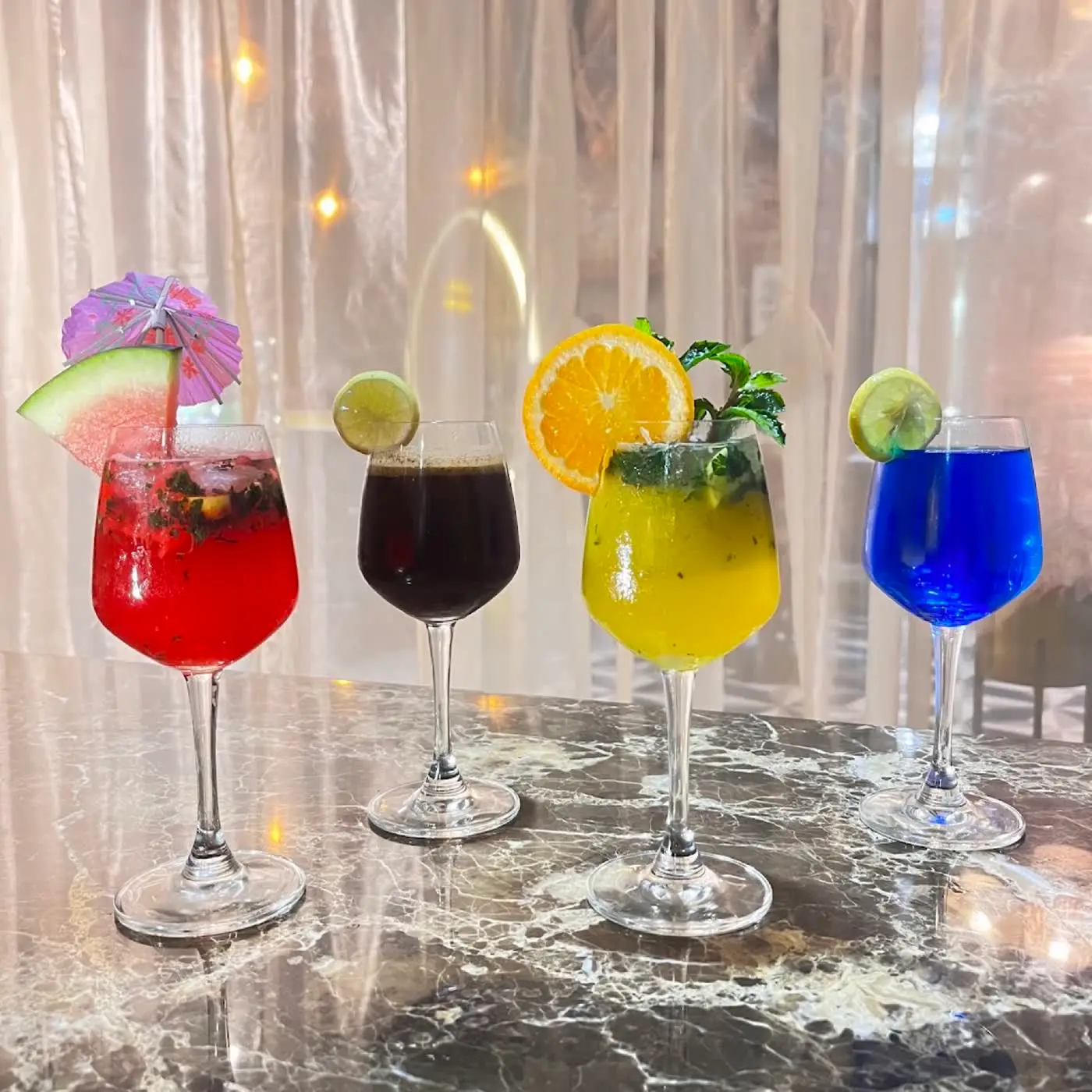 Four colourful mocktails garnished with fruit on a marble table