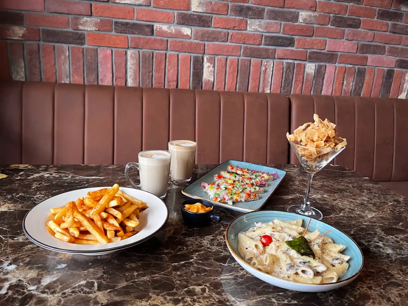 White sauce pasta, fries, nachos and cold coffee against a brick wall